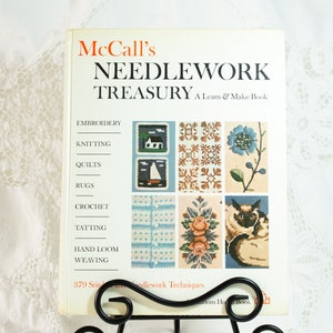 May include: A vintage McCall's Needlework Treasury book with a Learn & Make Book subtitle. The cover features illustrations of various needlework techniques, including embroidery, knitting, quilts, rugs, crochet, tatting, hand loom, and weaving.