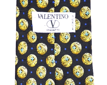 May include: A black silk tie with a repeating pattern of gold circles with blue and white accents. The tie has a blue lining with a repeating pattern of the Valentino logo. The tie has a label that reads "VALENTINO - CRAVATTE - MADE IN ITALY."