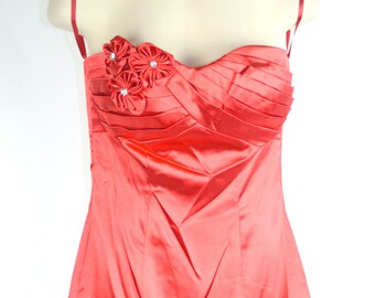 May include: A red satin strapless dress with a ruffled hem and floral embellishments. The dress has a fitted bodice and a flowing skirt.