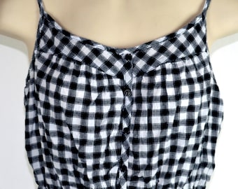 May include: A black and white gingham sleeveless top with a button down front and a ruffled hem.