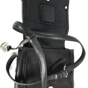 Może przedstawiać: Czarna sk&oacute;rzana torba na ramię z klapką. Torba posiada długi, regulowany pasek, srebrną klamrę i zawieszkę w kształcie serca. Wnętrze jest wyłożone czarną tkaniną i zawiera małą sk&oacute;rzaną metkę.