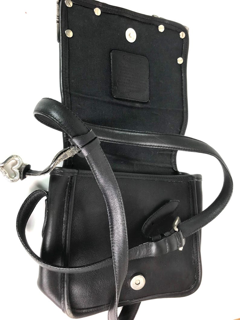 Może przedstawiać: Czarna sk&oacute;rzana torba na ramię z klapką. Torba posiada długi, regulowany pasek, srebrną klamrę i zawieszkę w kształcie serca. Wnętrze jest wyłożone czarną tkaniną i zawiera małą sk&oacute;rzaną metkę.