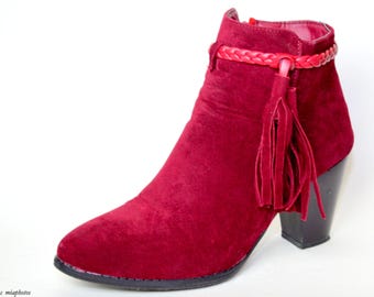 May include: Burgundy suede ankle boots with a tassel and a braided strap around the ankle. The boots have a block heel.