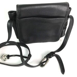Może przedstawiać: Czarna sk&oacute;rzana torba na ramię z klapką i przednią kieszenią. Torba posiada długi, regulowany pasek ze srebrną klamrą i zawieszką w kształcie serca.