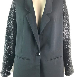 May include: A black blazer with long sleeves. The sleeves are covered in silver sequins.