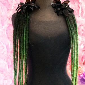 May include: Green synthetic dreadlocks with black fabric flower accents on a black mannequin. The mannequin is wearing a black shirt. The text "Diva Dreads" is visible at the bottom of the image.