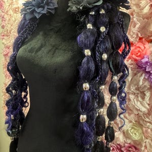 May include: A dark blue and black hair accessory with silver beads and dark blue fabric flowers. The hair piece is displayed on a black mannequin. The background is a wall of pink and purple paper flowers.