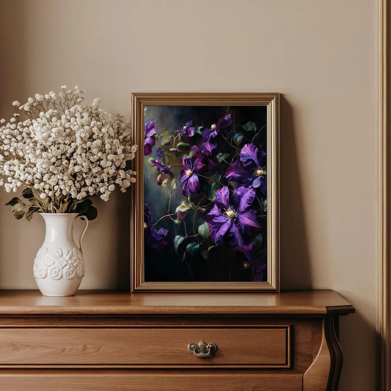 May include: A framed floral print featuring vibrant purple clematis flowers with yellow centers and green leaves. The artwork is set against a dark background, framed in gold, and displayed on a wooden dresser. A white vase with white flowers is on the left.