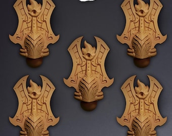 Puede incluir: Cinco hombreras de resina de color tostado idénticas que presentan un motivo de llama central y paneles geométricos intrincados. Cada pieza muestra un diseño de armadura esculpido con una base redondeada y un emblema de llama. La palabra Koi está impresa en blanco.
