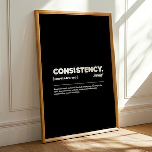 Puede incluir: Un marco negro con la palabra "CONSISTENCY" en blanco, junto con su pronunciación y definición. El marco es de color marrón claro. La impresión está apoyada contra una pared blanca y un suelo de madera.