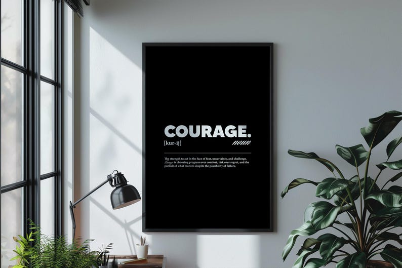 May include: Black framed wall art with the word "COURAGE" in white, along with its pronunciation and definition. The art is displayed on a white wall, next to a window and a potted plant.