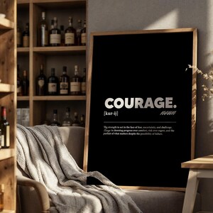 May include: A framed black print with the word "COURAGE" in white, with the definition below. The print is displayed in a room with a wooden bookshelf and a neutral-colored blanket draped over a chair.