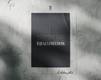 May include: Black poster with the text "DISCIPLINE EQUALS FREEDOM" in white, hanging on a textured gray wall. The poster has a wrinkled appearance. The phrase "For Ambitious Minds" is at the bottom.