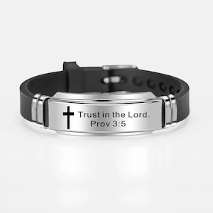 May include: Black silicone bracelet with a silver metal plate. The plate features a black cross and the text "Trust in the Lord. Prov 3:5". The bracelet has a buckle fastening.