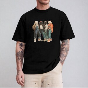 Puede incluir: Camiseta negra con un gr&aacute;fico de cuatro gatos vestidos con ropa urbana. Los gatos llevan monos vaqueros, chaquetas y zapatillas deportivas. La imagen tiene un estilo vintage y de dibujos animados.