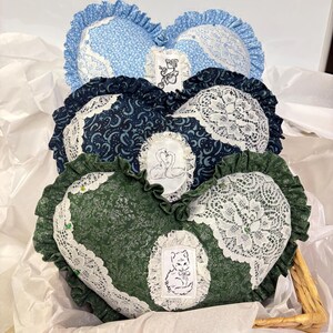 Peut inclure: Coussins décoratifs en forme de cœur bleus, marine et verts, chacun avec une bordure en dentelle blanche et des bords à volants. Les coussins présentent des tissus à motifs floraux, célestes et à motifs. Chaque coussin a un petit patch brodé avec un chat, des cygnes ou des fleurs.