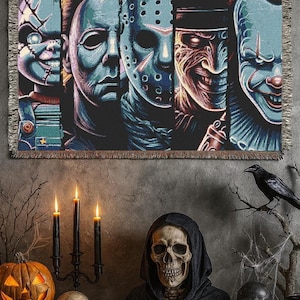 Può includere: Una coperta tessuta con un collage di personaggi di film horror, tra cui Chucky, Michael Myers, Jason Voorhees, Freddy Krueger e Pennywise. La coperta ha un bordo con frange ed è principalmente nera, blu e rossa. La coperta è esposta sopra una scena di Halloween.