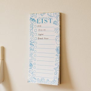 Könnte beinhalten: Ein rechteckiger Einkaufszettel-Notizblock mit blauem Rand und Text. Der Notizblock hat einen blauen Titel "Grocery List" und eine Liste von Artikeln, darunter Milch, Olivenöl, Äpfel und Brotmehl. Der Notizblock ist mit blauen Illustrationen von Lebensmitteln verziert.