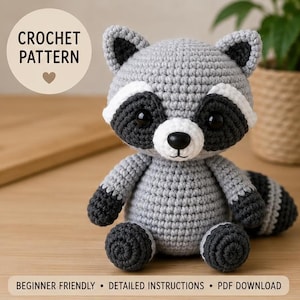 May include: A gray and white crocheted raccoon plush toy with black eye patches, a black nose, and a striped tail. The image includes the text CROCHET PATTERN, BEGINNER FRIENDLY, DETAILED INSTRUCTIONS, and PDF DOWNLOAD on a light background.