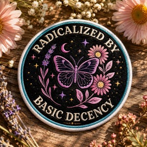 May include: A circular embroidered patch with a black background featuring a purple butterfly, pink flowers, and lavender sprigs. The text "RADICALIZED BY BASIC DECENCY" is stitched in white capital letters along the top and bottom edges.