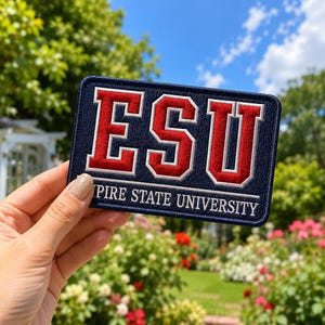 May include: A rectangular embroidered patch with a dark navy blue background and a white border. The patch features the large red letters ESU with white outlines, and the text EMPIRE STATE UNIVERSITY in white capital letters below.