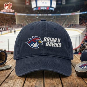 May include: A navy blue baseball cap with the text "Briar U Hawks" embroidered in white. The cap features a logo of a hawk in red, blue, and white. The hat is displayed on a wooden surface.
