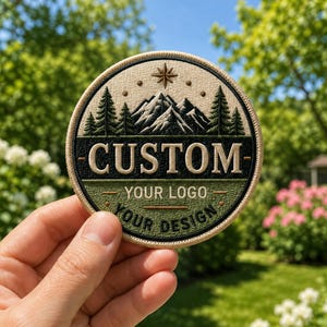 Peut inclure: Un écusson brodé circulaire représentant une chaîne de montagnes et des sapins au-dessus d'une bande horizontale noire avec le texte CUSTOM. En dessous, une section verte affiche le texte YOUR LOGO et YOUR DESIGN avec une étoile en haut.