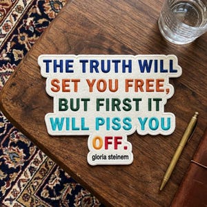 May include: A white felt patch with embroidered text that reads: THE TRUTH WILL SET YOU FREE, BUT FIRST IT WILL PISS YOU OFF. The words are stitched in blue, orange, green, and teal, with the word OFF in orange and red, followed by gloria steinem.