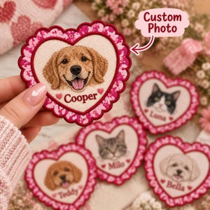 Op de afbeelding: Een hartvormige geborduurde patch met een gedetailleerd portret van een golden retriever met de naam Cooper eronder geborduurd. De patch heeft een geschulpte rand met een roze en wit bloemenpatroon en een donkerrode rand.