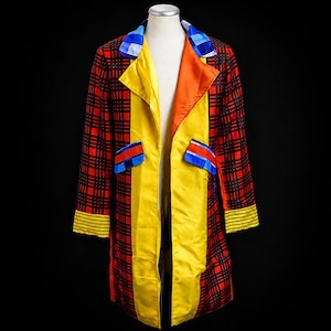 May include: A long coat featuring a red and black plaid pattern on the sleeves and back, with solid yellow front panels, an orange lapel, and a blue and white checkered collar. The coat includes two pockets with blue and red flaps and yellow striped cuffs.