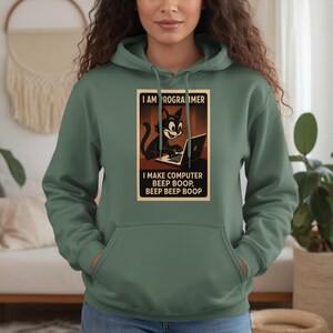 May include: Sage green hoodie with a graphic of a black cat using a laptop. The graphic includes the text: "I AM PROGRAMMER, I MAKE COMPUTER BEEP BOOP, BEEP BEEP BOOP."