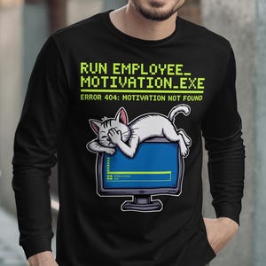 May include: Black long-sleeved top featuring a cartoon cat resting on a computer screen. The text reads "RUN EMPLOYEE_ MOTIVATION_EXE" and "ERROR 404: MOTIVATION NOT FOUND" in green and white.