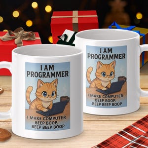 Könnte beinhalten: Zwei weiße Keramikbecher mit einem Cartoon-Katzen-Design. Die Katze trägt eine Brille und arbeitet an einem Laptop. Auf den Bechern steht "I AM PROGRAMMER" und "I MAKE COMPUTER BEEP BOOP, BEEP BEEP BOOP". Die Becher stehen auf einer Holzoberfläche mit Weihnachtsdekorationen.