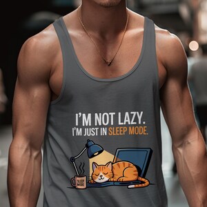 Puede incluir: Camiseta sin mangas gris con el texto "I'M NOT LAZY. I'M JUST IN SLEEP MODE." Un gato de dibujos animados está durmiendo en un portátil junto a una lámpara y una taza de café. El gato es naranja con rayas marrones.