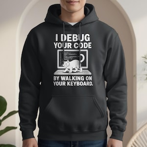 Könnte beinhalten: Schwarzer Kapuzenpullover mit dem Text "I Debug Your Code By Walking On Your Keyboard". Das Design zeigt einen Laptop mit Code auf dem Bildschirm und eine weiße Katze, die über die Tastatur läuft. Der Hoodie hat eine Vordertasche und eine Kapuze mit Kordelzug.
