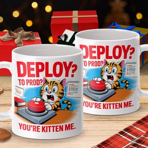 May include: Two white ceramic mugs with the text "DEPLOY? TO PROD? YOU'RE KITTEN ME." feature a cartoon cat pressing a red button. The mugs are on a wooden surface with gift boxes and a gingerbread man in the background.
