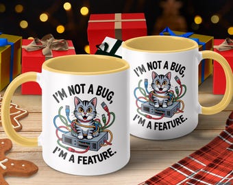 Op de afbeelding: Witte keramische mok met een gele handgreep en binnenkant. De mok heeft een cartoon kattenontwerp met de tekst "I'M NOT A BUG, I'M A FEATURE." De kat is omringd door kleurrijke kabels, tegen een feestelijke achtergrond.