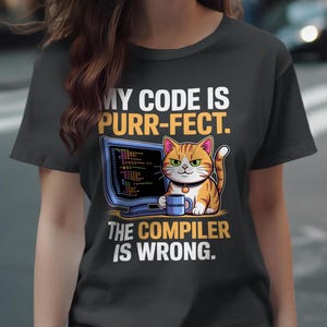May include: Dark grey t-shirt featuring a cartoon cat and computer design. The cat is orange and white, holding a mug, and the text reads "MY CODE IS PURR-FECT. THE COMPILER IS WRONG."