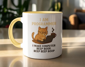 Op de afbeelding: Witte keramische mok met een gele handgreep en binnenkant. De mok heeft een cartoonkat met een bril die op een laptop werkt, met de tekst "I AM PROGRAMMER" en "I MAKE COMPUTER BEEP BOOP, BEEP BEEP BOOP".