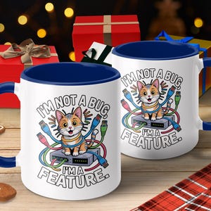 May include: White ceramic mug with a blue interior and handle. The mug features a cartoon cat illustration with the text "I'M NOT A BUG, I'M A FEATURE." Colorful network cables surround the cat. The background includes gift boxes.