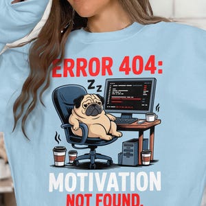 May include: Light blue sweatshirt with a graphic of a pug sleeping in an office chair in front of a computer. The text reads "ERROR 404: MOTIVATION NOT FOUND." Coffee cups and a computer tower are also visible.
