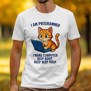 May include: White t-shirt with a cartoon orange tabby cat using a blue laptop. The text above the cat says "I AM PROGRAMMER", and below it, "I MAKE COMPUTER BEEP BOOP, BEEP BEEP BOOP".