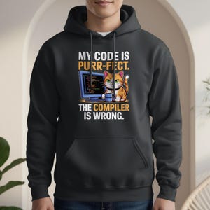 Puede incluir: Sudadera con capucha negra con un gráfico frontal que presenta un gato de dibujos animados con una computadora y el texto "MY CODE IS PURR-FECT. THE COMPILER IS WRONG."
