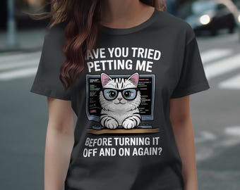 May include: Dark grey t-shirt with a cartoon cat wearing glasses in front of a computer screen. The text on the shirt reads "HAVE YOU TRIED PETTING ME BEFORE TURNING IT OFF AND ON AGAIN?"