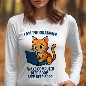 May include: White long-sleeved top featuring a cartoon orange tabby cat working on a blue laptop. The text above the cat reads "I AM PROGRAMMER", and below it, "I MAKE COMPUTER BEEP BOOP, BEEP BEEP BOOP".