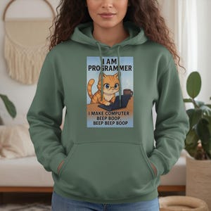 May include: Green hooded sweatshirt featuring a graphic of an orange cat wearing glasses and working on a laptop. The text on the graphic reads "I AM PROGRAMMER" and "I MAKE COMPUTER BEEP BOOP. BEEP BEEP BOOP."