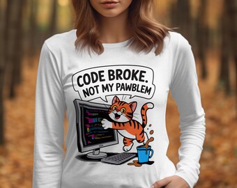 May include: White long-sleeved top featuring a cartoon cat and computer graphic. The cat is orange and white, and the computer screen displays code. Text reads "CODE BROKE. NOT MY PAWBLEM" in a speech bubble.