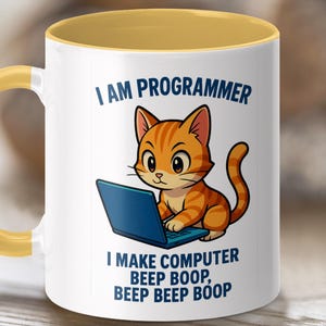 Könnte beinhalten: Weiße Keramik-Tasse mit gelbem Henkel und Innenraum. Die Tasse zeigt eine Cartoon-orangefarbene Tabby-Katze, die an einem blauen Laptop arbeitet. Der Text auf der Tasse lautet "I AM PROGRAMMER" und "I MAKE COMPUTER BEEP BOOP, BEEP BEEP BOOP."