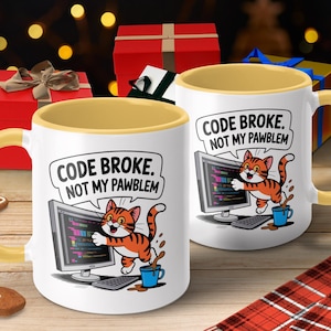 Peut inclure: Mug en céramique blanche avec une anse et un intérieur jaunes. La tasse présente un chat de dessin animé avec le texte "CODE BROKE. NOT MY PAWBLEM" et un écran d'ordinateur. Une tasse à café bleue et un clavier sont également représentés.