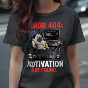 May include: Dark gray t-shirt with a graphic of a pug sleeping in an office chair in front of a computer. The text reads "ERROR 404: MOTIVATION NOT FOUND." Coffee cups and office supplies are also visible.